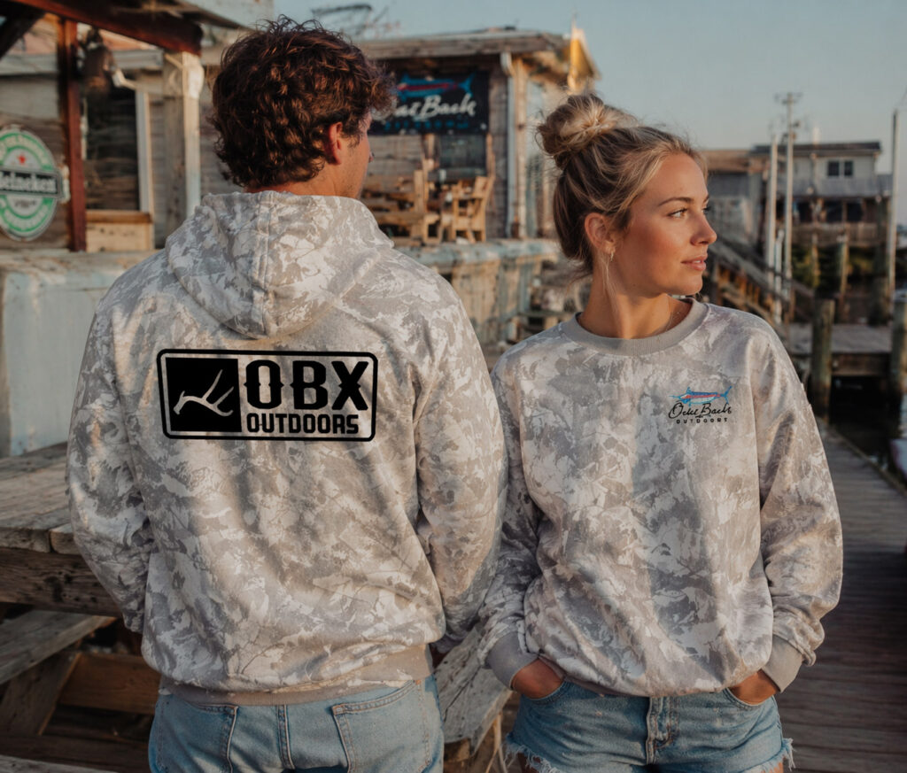 Two individuals in camouflage hoodies stand together on a dock