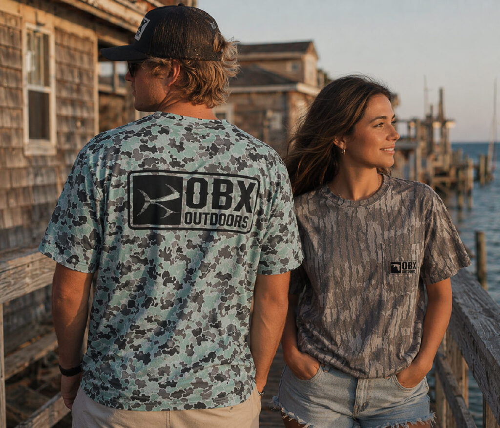 A man and woman pose on a dock, showcasing their "OBX" branded shirts.